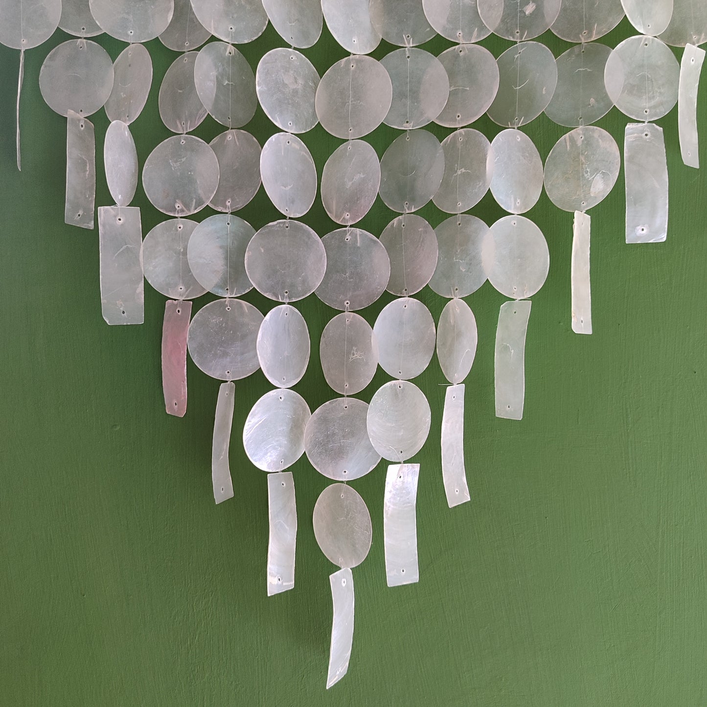 Decorative chandelier with white tound and rectangular capiz shell against a green wall