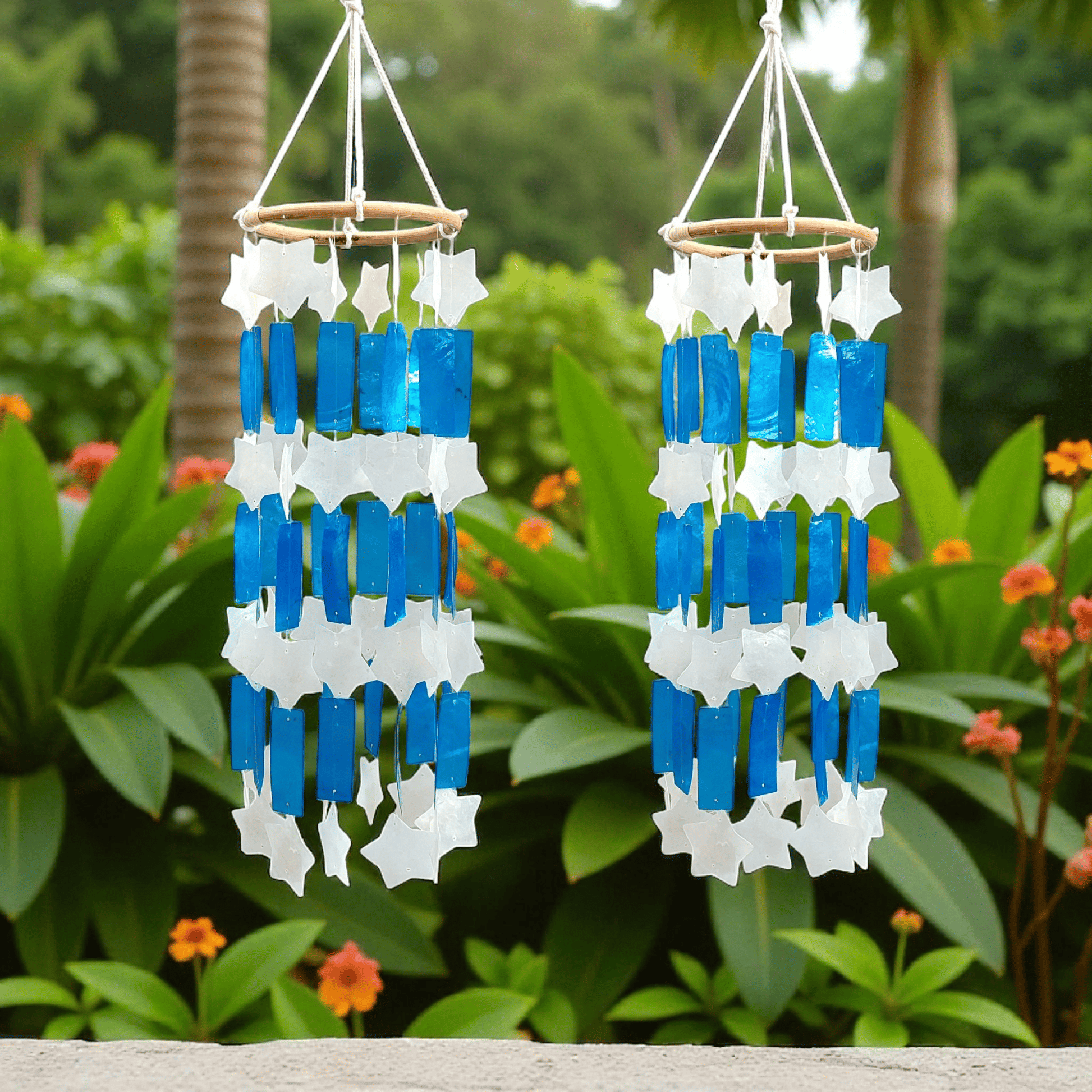 Two wind chimes with blue and white star-shaped shell hanging against a green garden background.
