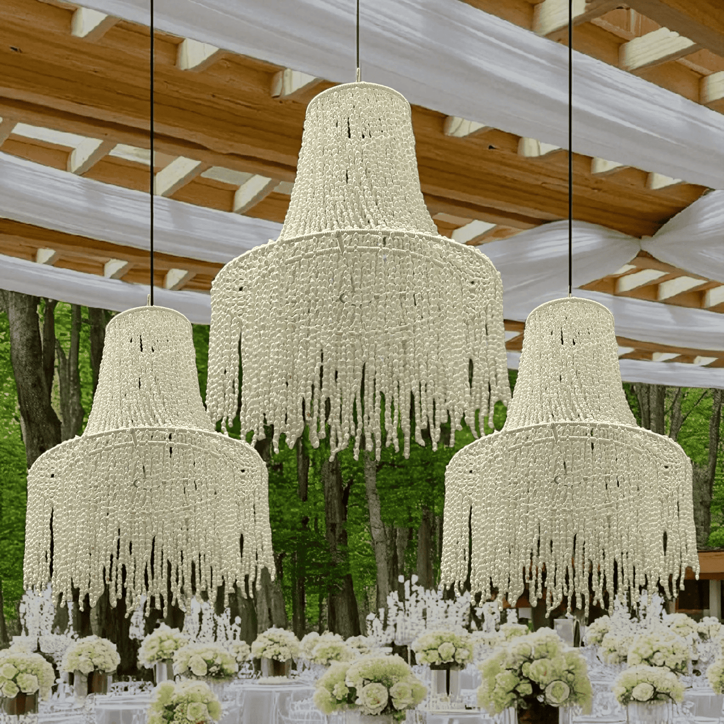 Three large chandeliers hanging from a wooden ceiling with floral arrangements on tables below in coastal wedding decor