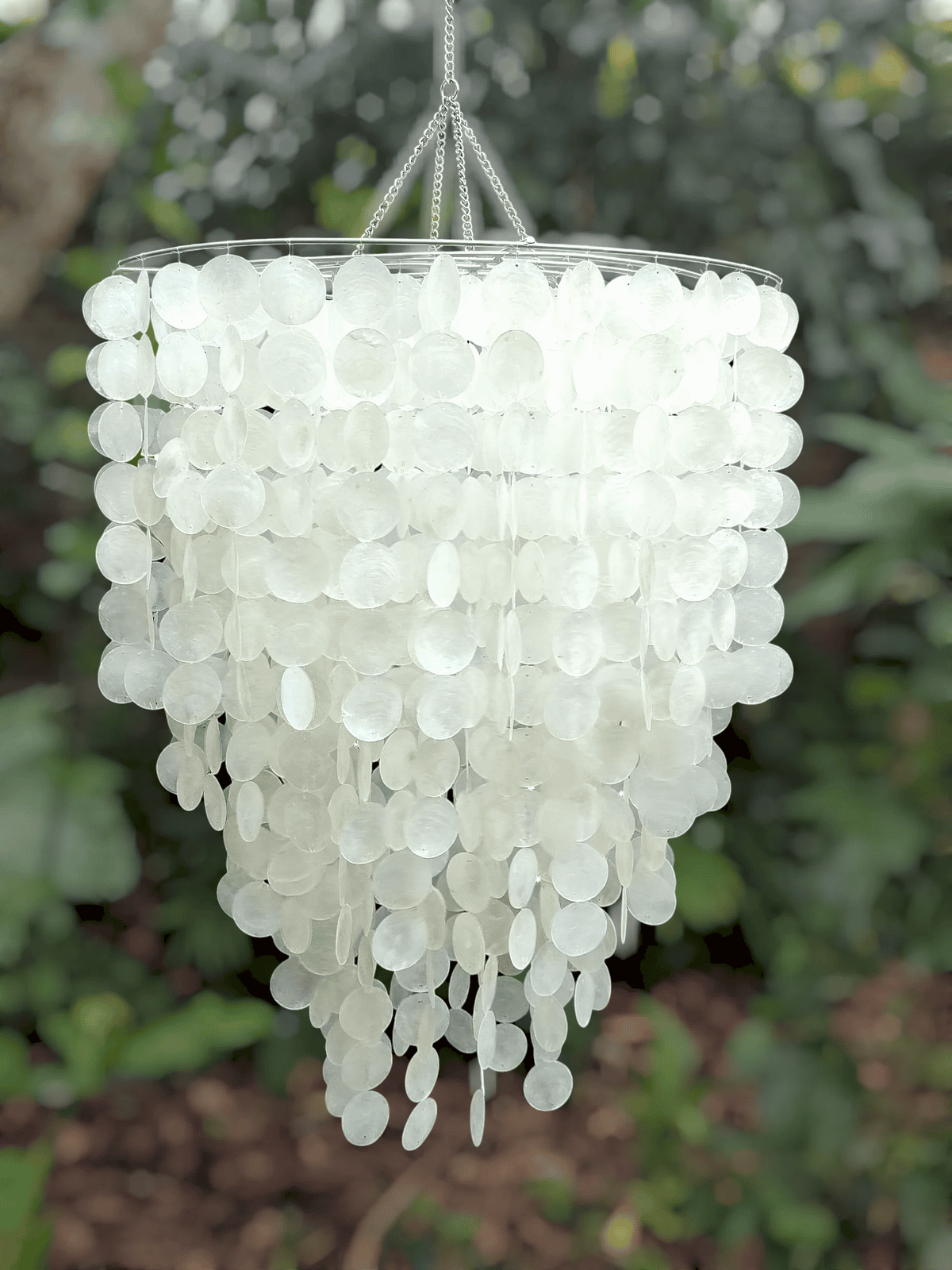 White capiz shell chandelier hanging against a blurred green outdoor background