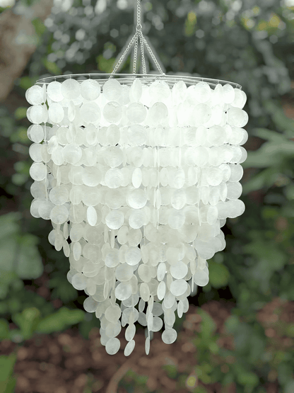 White capiz shell chandelier hanging against a blurred green outdoor background