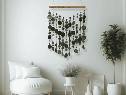 Black capiz shell wall hanging in a room with a white wall, plant, and chair.