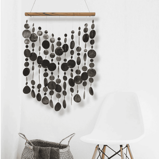 Capiz shell wall hanging with black circular patterns on a white background