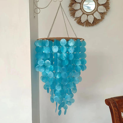 Blue hanging capiz chandelier on a white wall with a mirror above it.