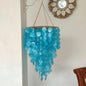 Blue hanging capiz chandelier on a white wall with a mirror above it.