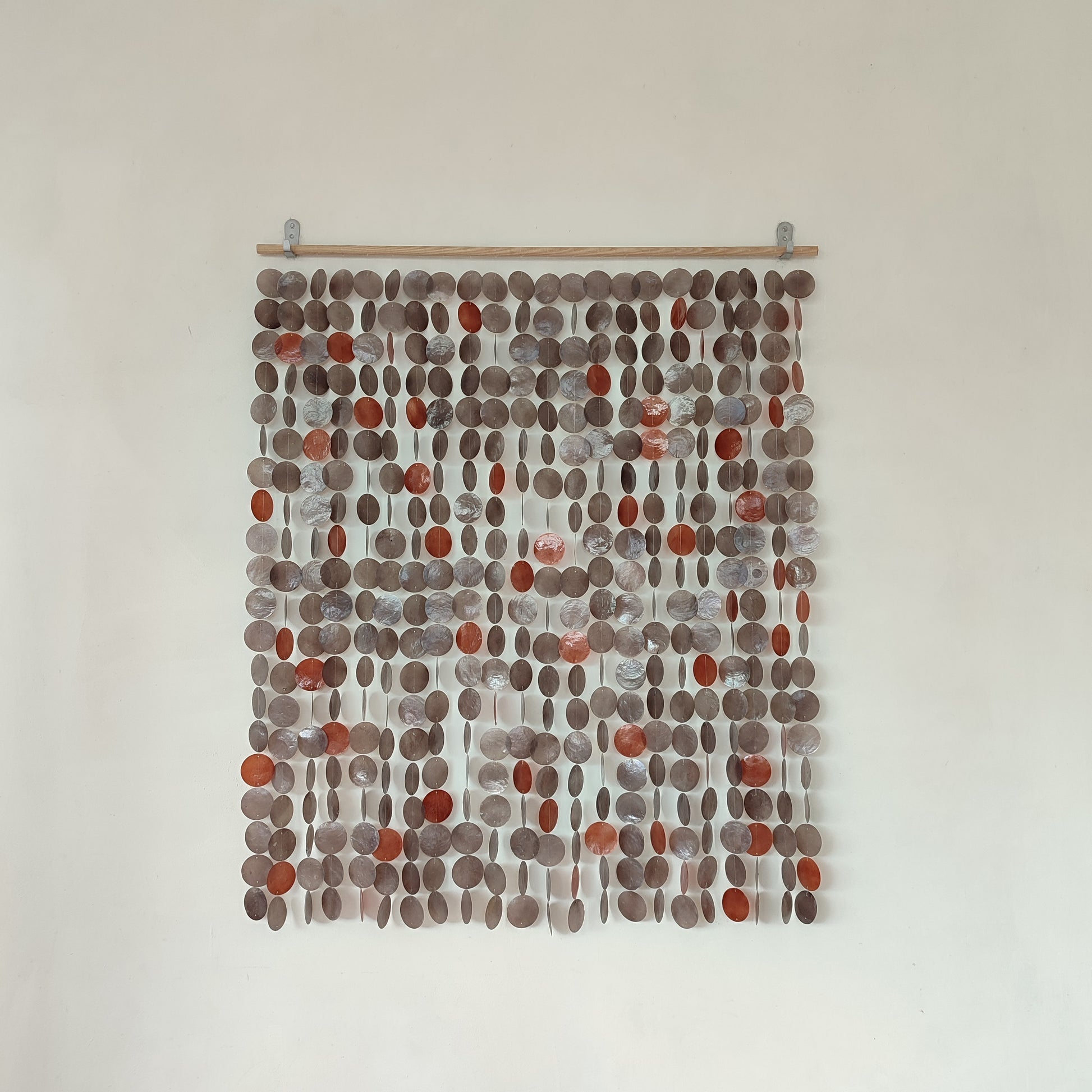 Textile art piece with circular patterns in brown and red on a white wall.