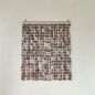 Textile art piece with circular patterns in brown and red on a white wall.