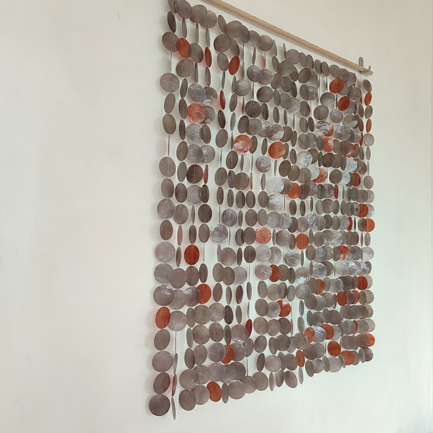 Textile wall art with circular patterns in shades of gray and brown on a white wall.