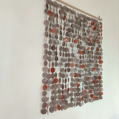Textile wall art with circular patterns in shades of gray and brown on a white wall.