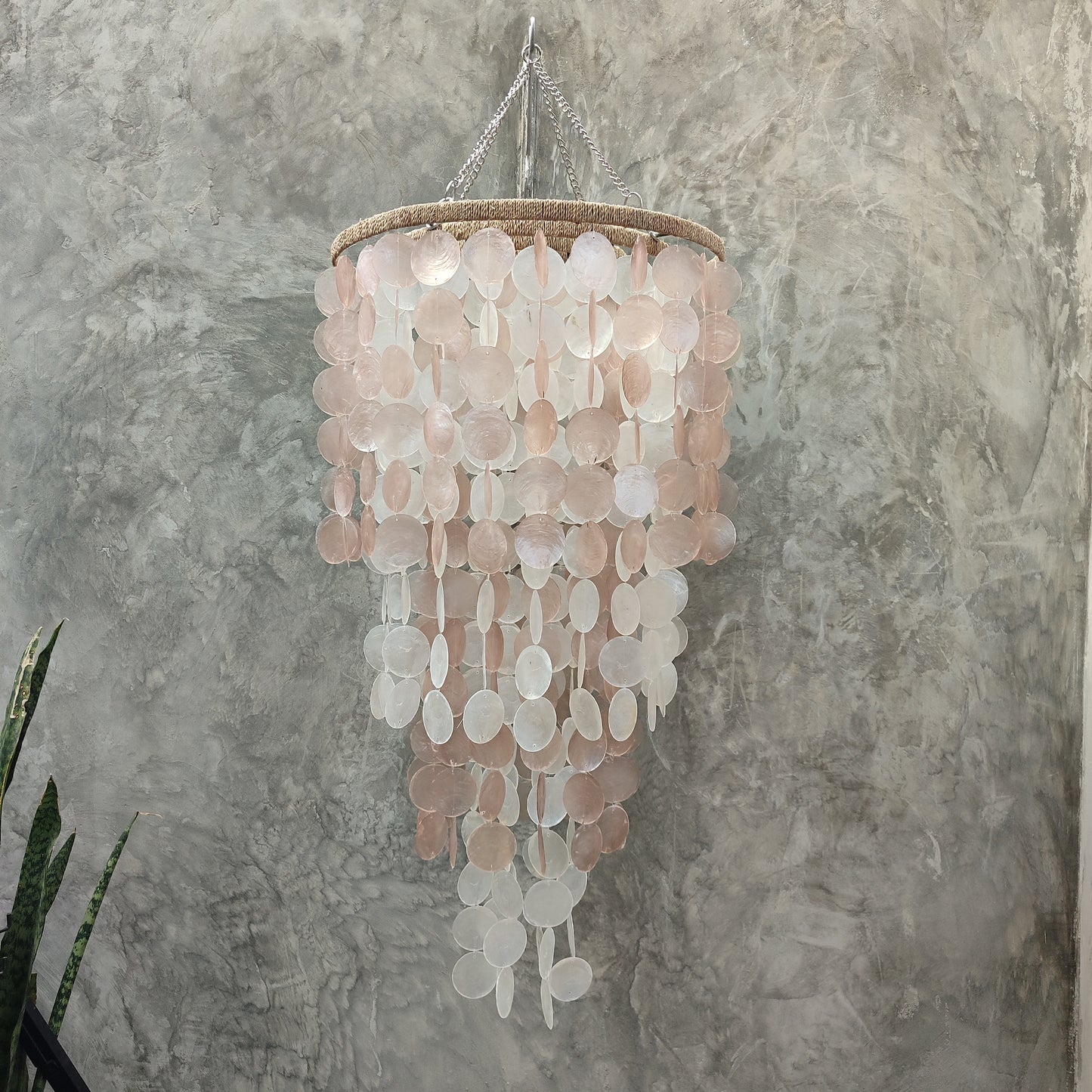 Chandelier made of circular pink and white discs against a textured gray wall.