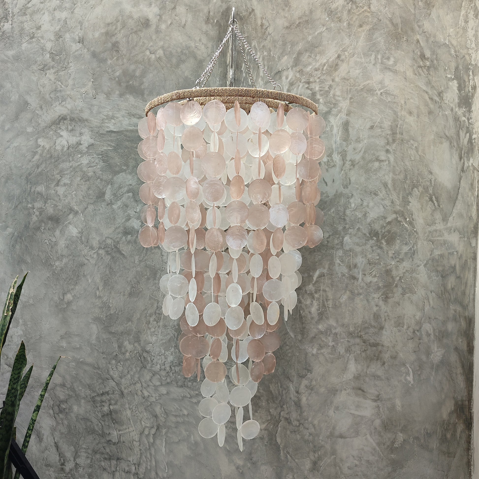 Chandelier made of circular pink and white discs against a textured gray wall.