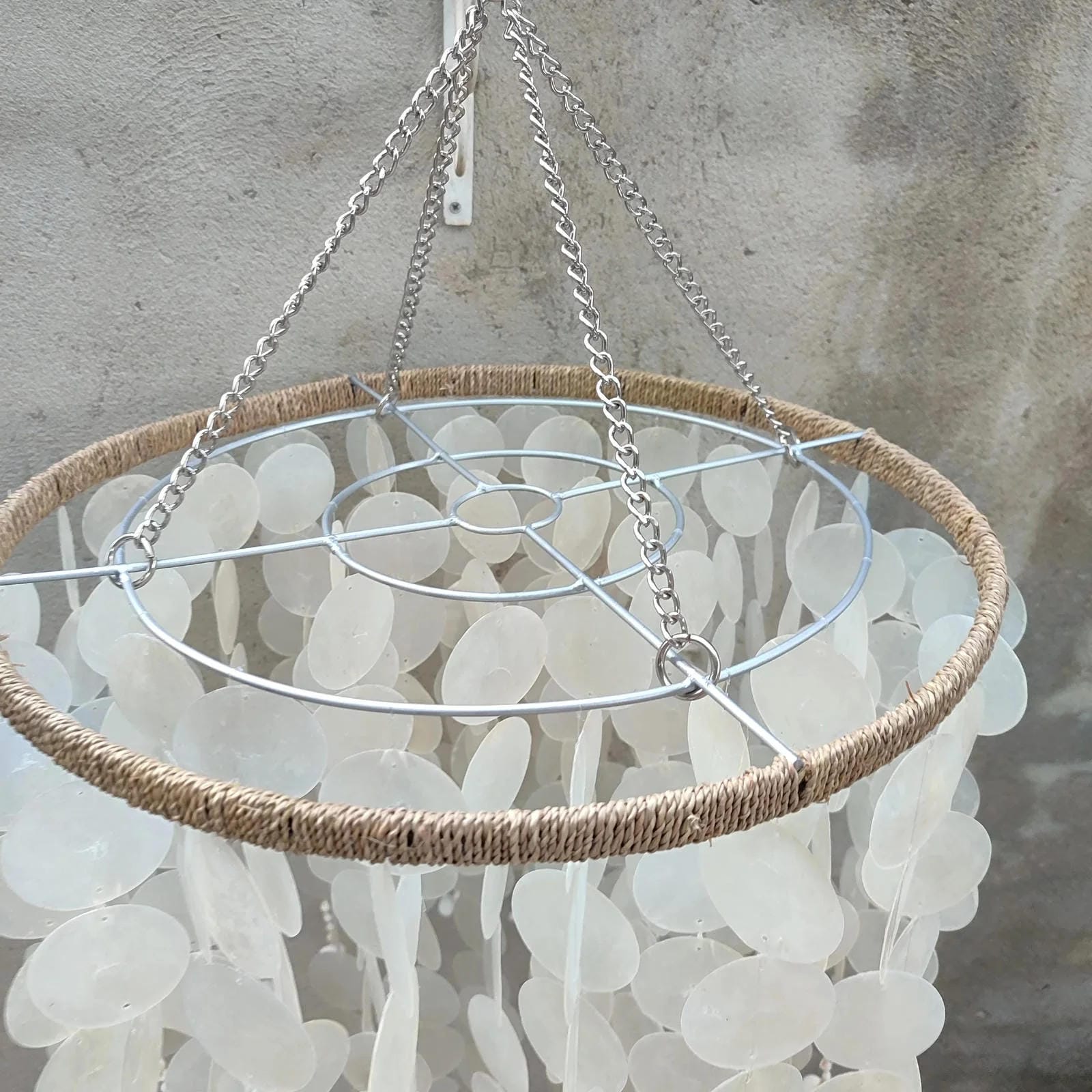 Capiz shell hanging light fixture with natural fiber rim against a textured wall.