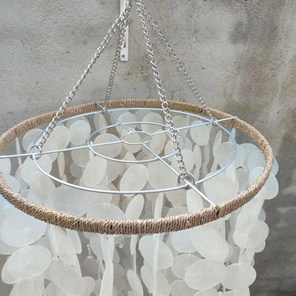 Capiz shlell chandelier light fixture with natural fiber rim and metal structure against a textured wall.