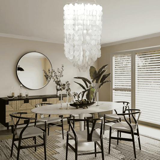 Dining room with a modern capiz shell chandelier, round mirror, and table setting.