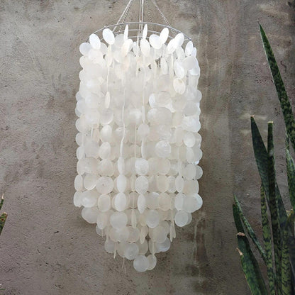 White capiz shell chandelier hanging against a textured wall with a cactus plant.