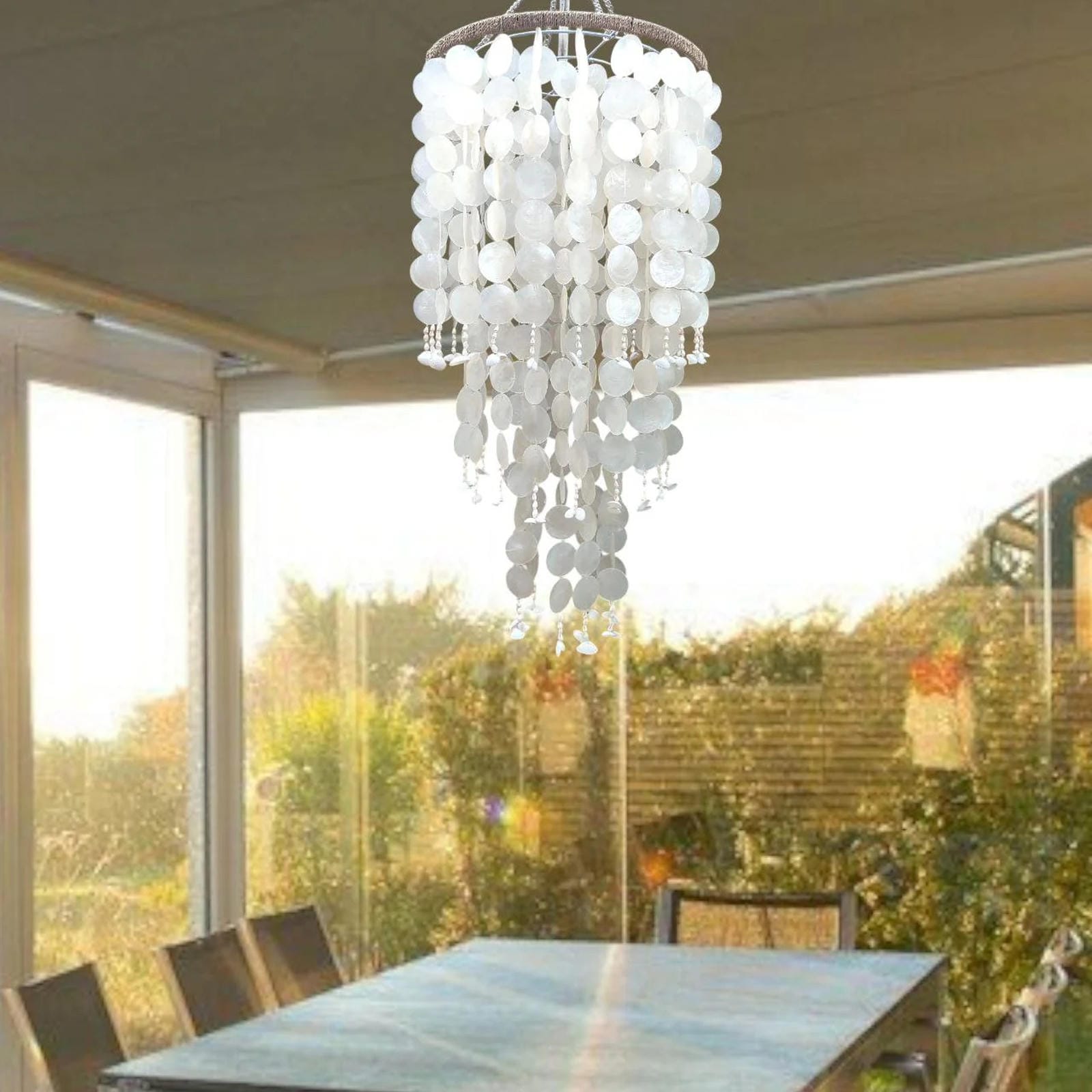 Cqpiz shell chandelier hanging above a dining table with a garden view