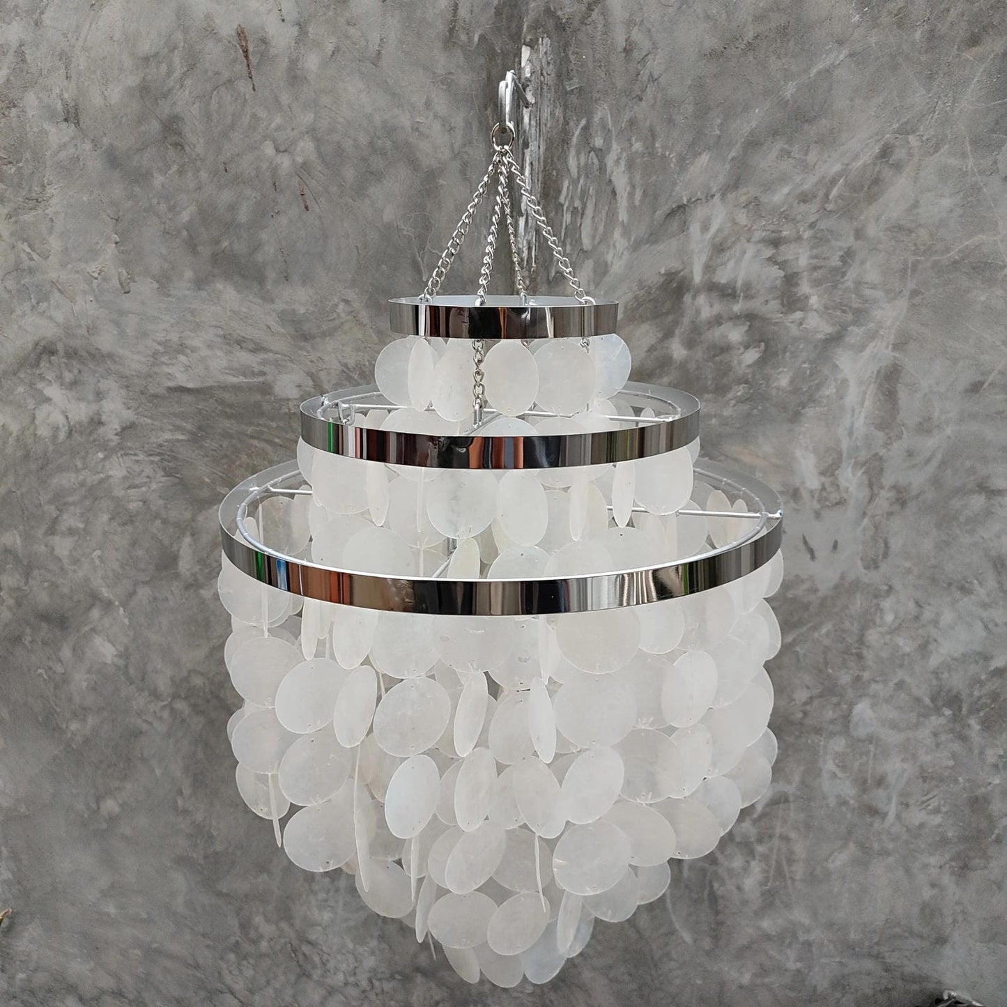 Chandelier with white capiz shell and chrome accents against a gray marble background