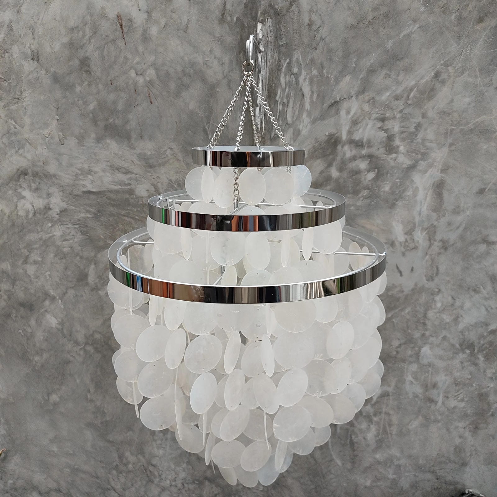 Chandelier with white capiz shell and chrome accents against a gray marble background