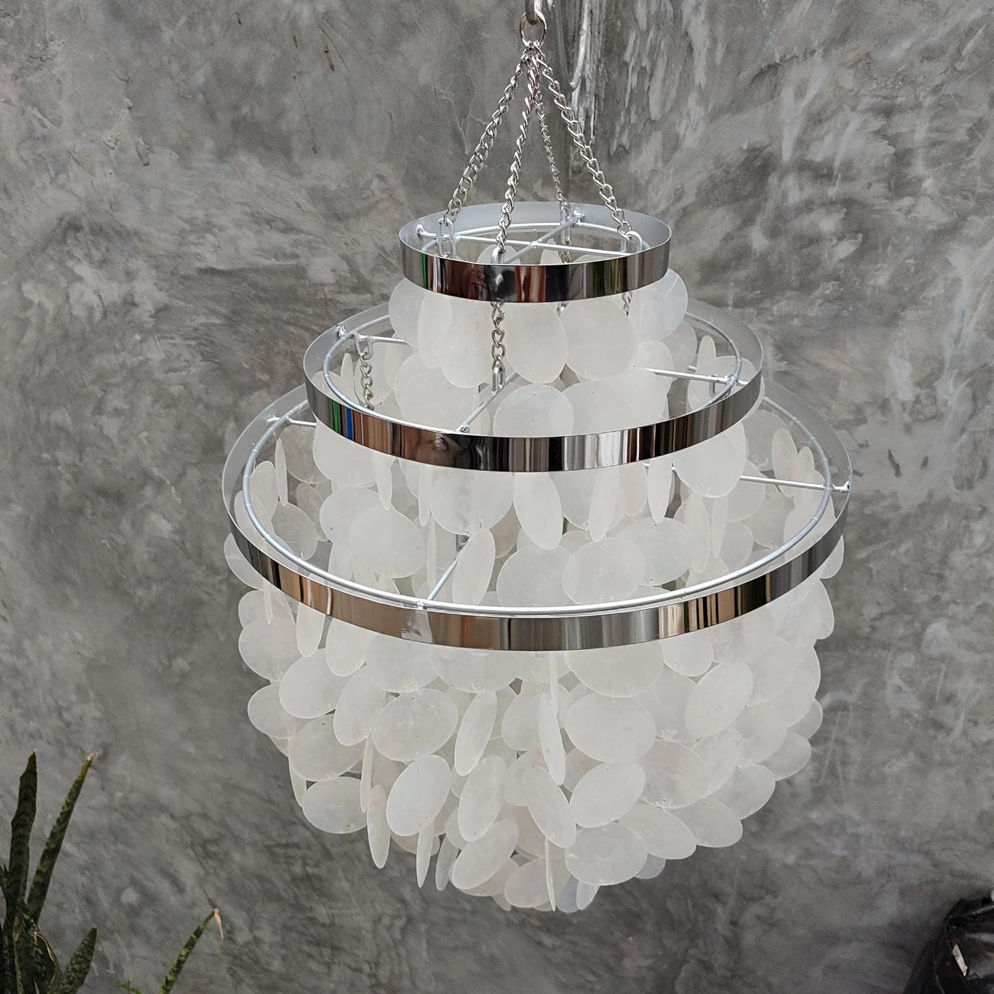 Chandelier with white round capiz shell and silver metal accents against a gray textured wall.