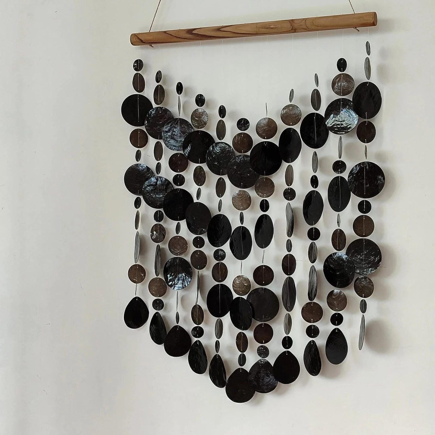 Capiz shell wall hanging with black circular elements on a white background