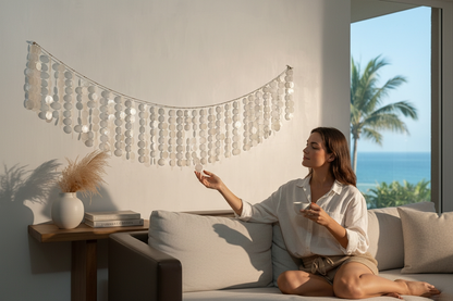 Woman sitting on a couch in a modern living room with capiz shell wall hanging and a view of the ocean