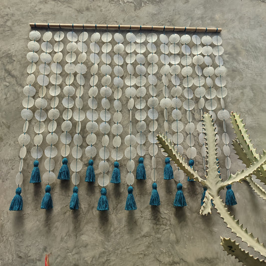 Decorative round capiz shell wall hanging  and blue tassels on a textured wall.