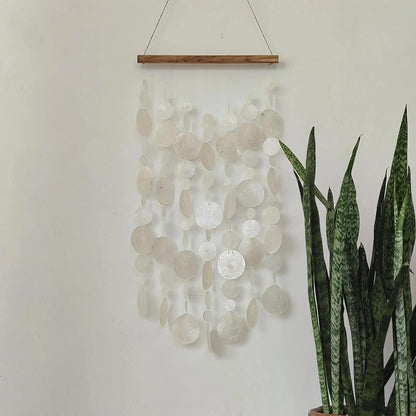 Decorative wall hanging with circular shell patterns on a plain wall next to a potted plant.