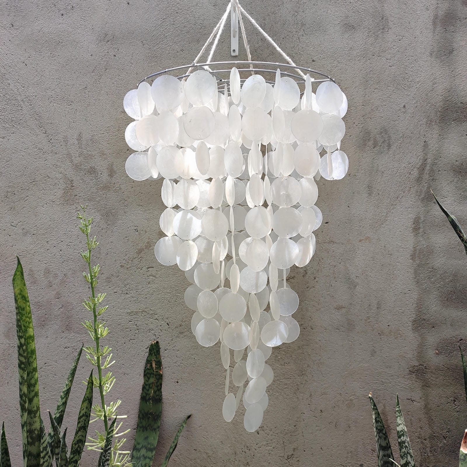 White capiz shell wind chime with circular elements against a textured wall.