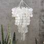 White capiz shell wind chime with circular elements against a textured wall.