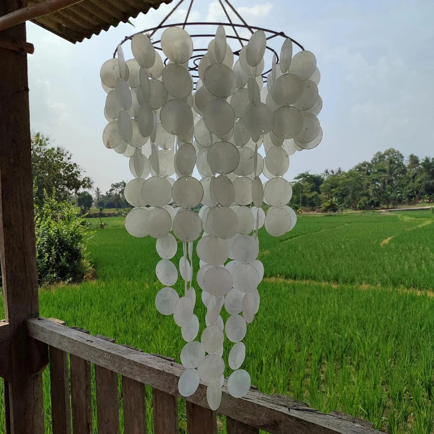 Decorative hanging wind chime with a scenic background of green fields and trees.