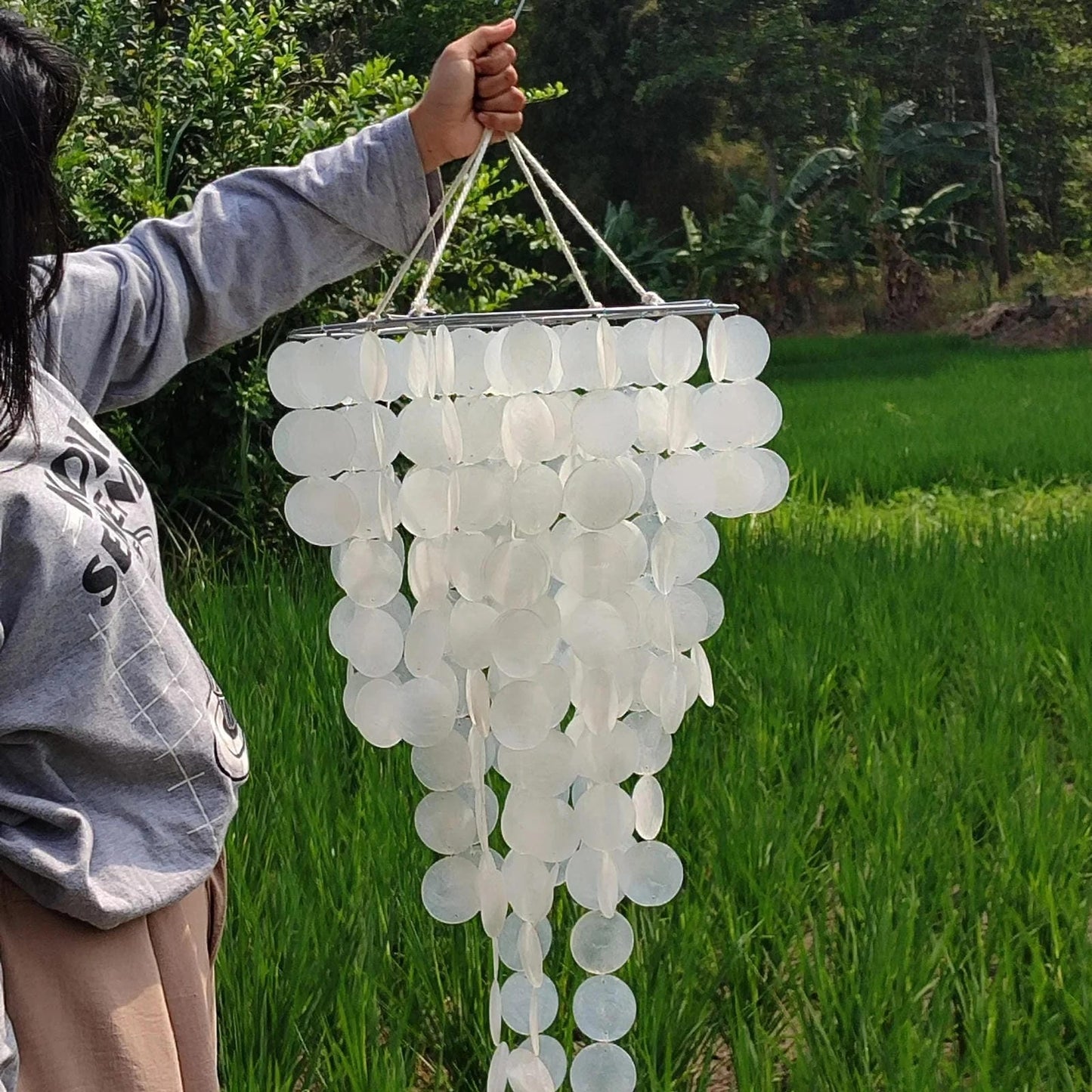 Person holding a white decorative hanging in a green outdoor setting
