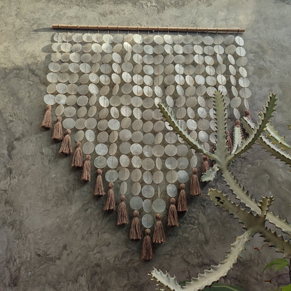 Decorative wall hanging made from capiz shell and tassels on a textured wall.