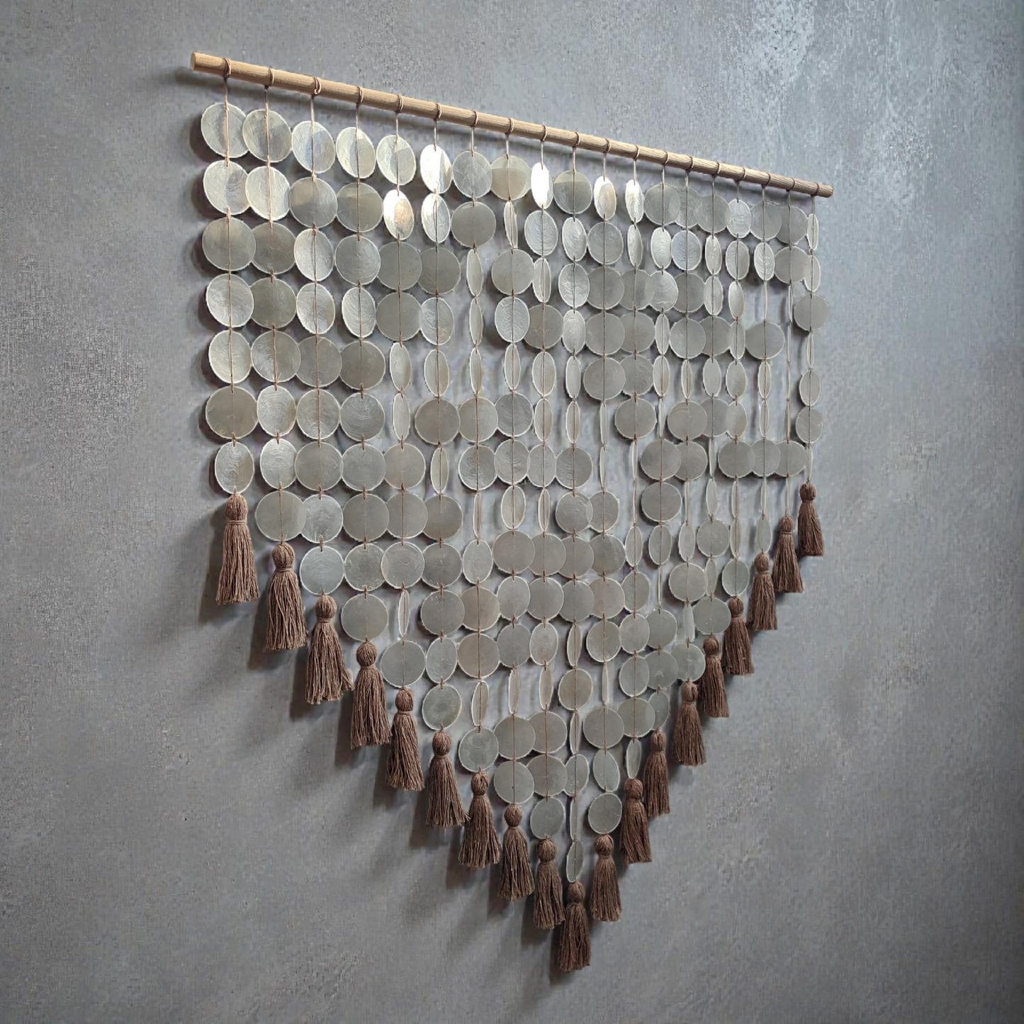 Decorative wall hanging made from capiz shell and tassels on a gray wall