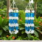 Two wind chimes with blue and white star-shaped shell hanging against a green garden background.