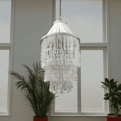 White shell chandelier with silver metal frame hanging in front of a window.
