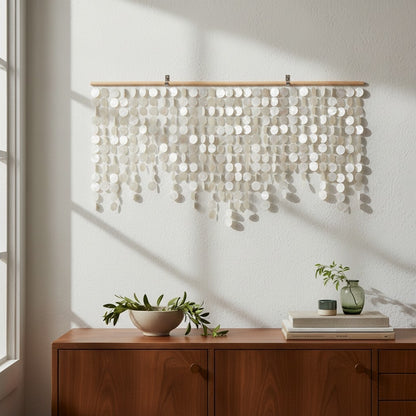 Decorative wall hanging with circular elements on a white wall above a wooden cabinet with plants and books.