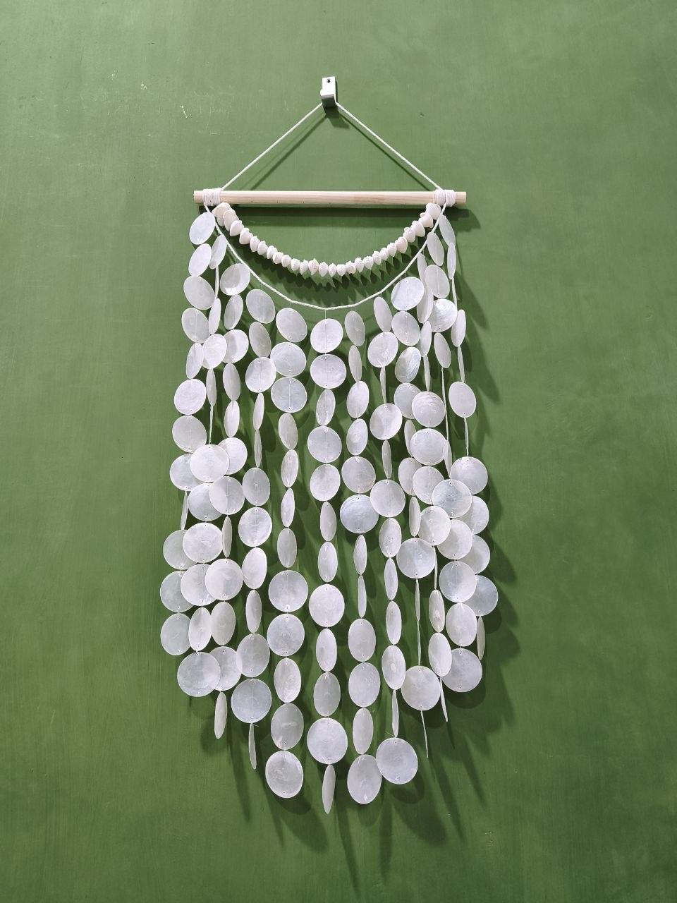 White decorative wall hanging with circular elements on a green background