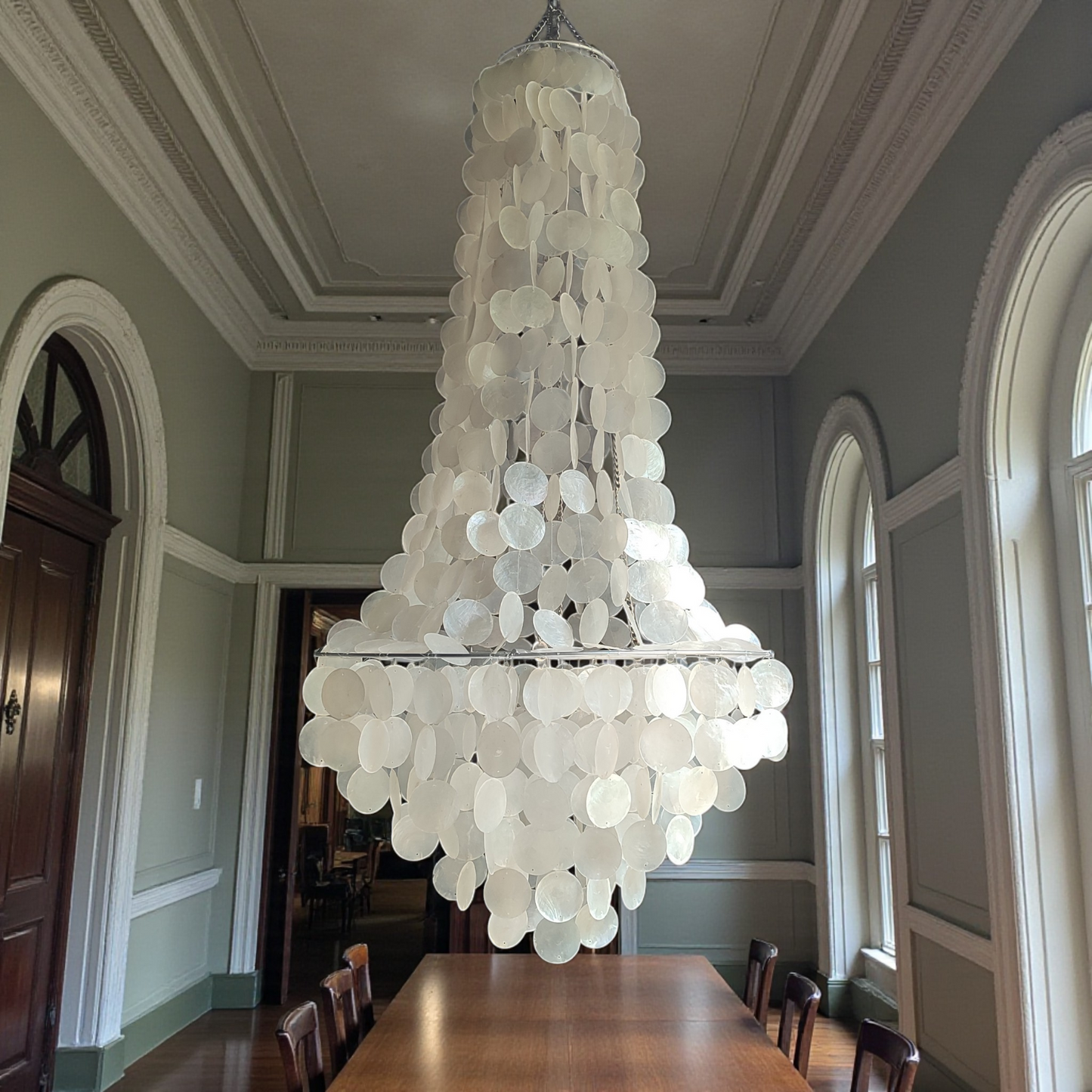 Large chandelier hanging in a room with a wooden table and chairs.