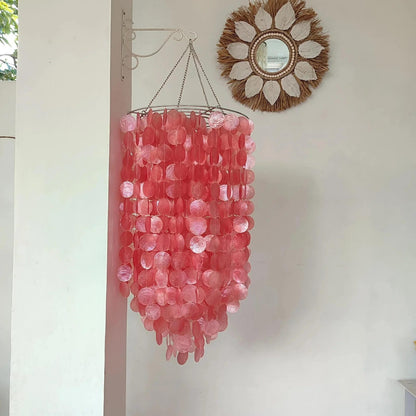 Pink chandelier hanging on a white wall with a decorative mirror above it.