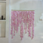 A pink disc bead curtain hanging from a wooden rod on a white wall, with decorative shelving visible on the left.