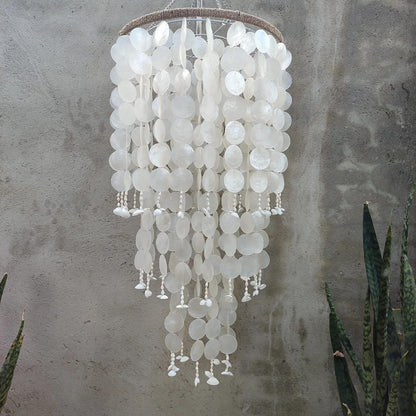 White capiz shell chandelier against a neutral wall with plants in the background