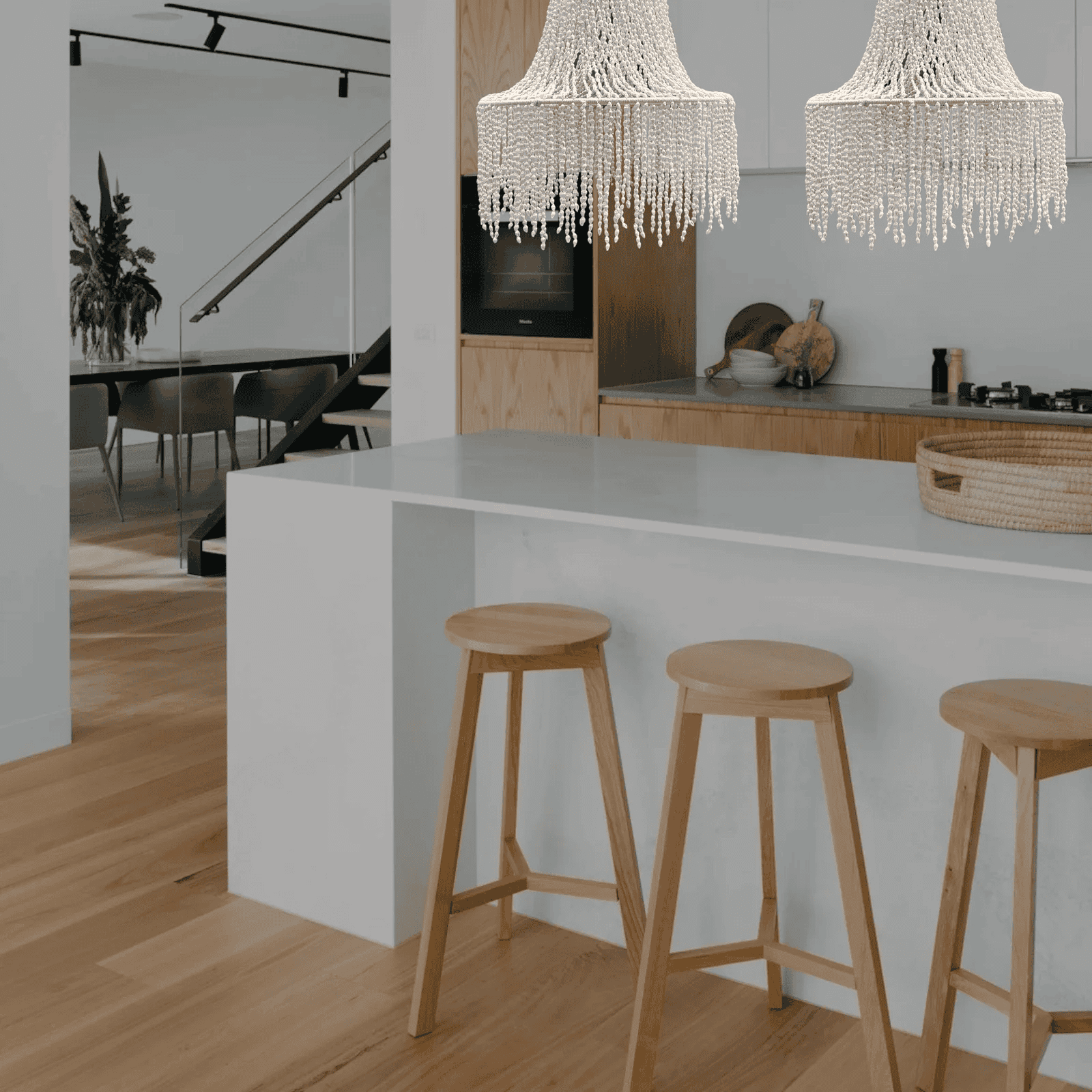 Modern kitchen with white island, wooden stools, and seashell chandeliers.