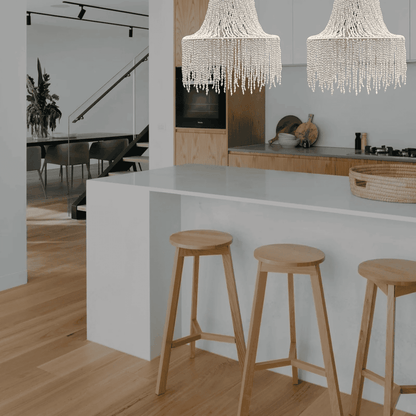 Modern kitchen with white island, wooden stools, and seashell chandeliers.