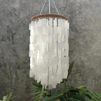 Chandelier made of white square capiz shell hanging against a gray marble wall.