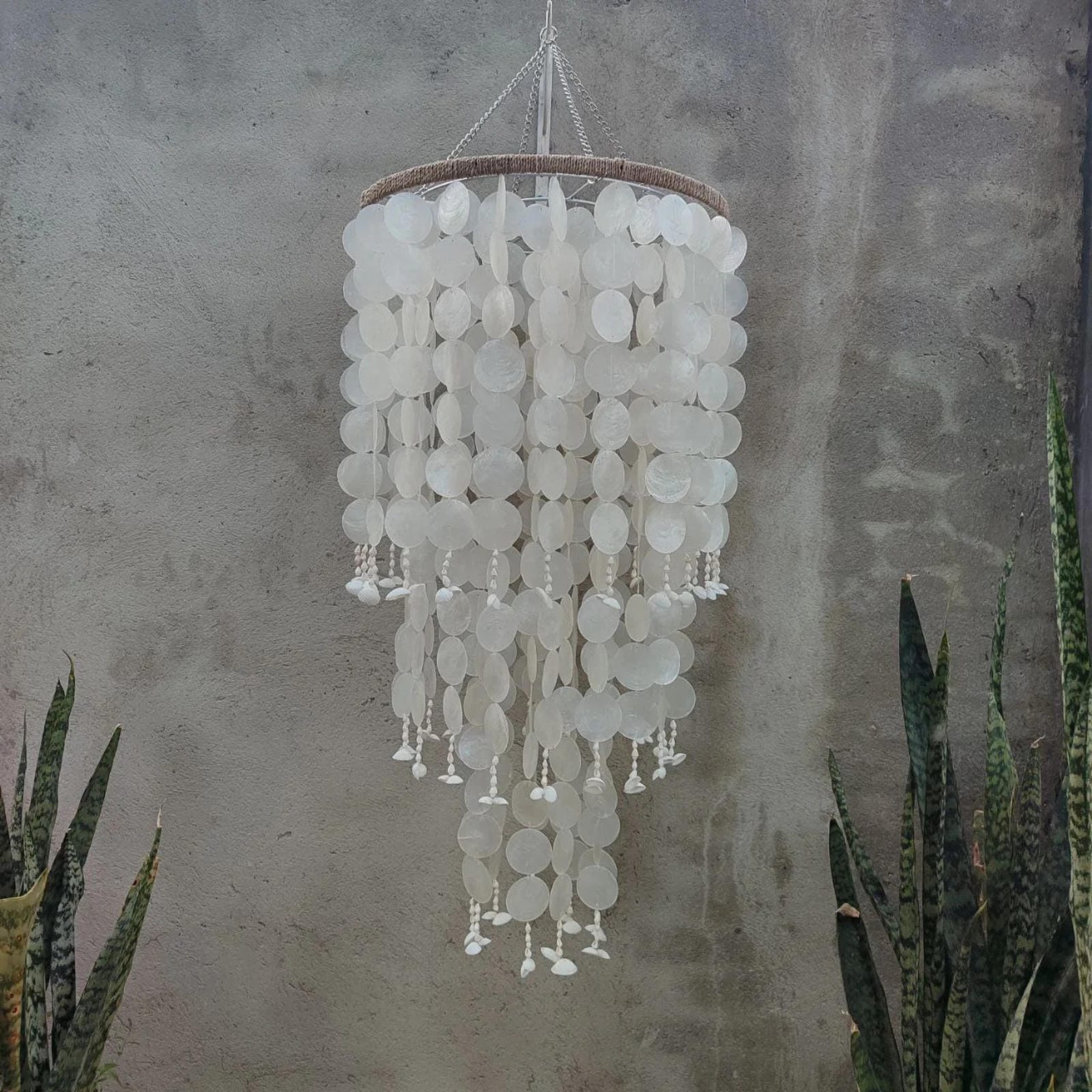 Decorative chandelier with white circular elements hanging against a textured wall.