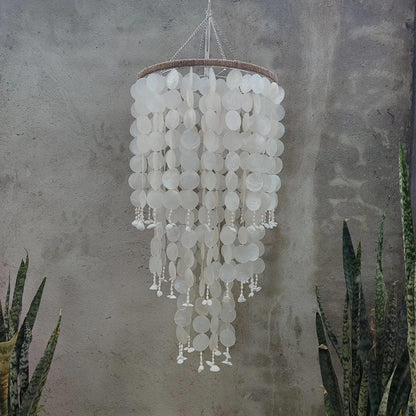 Decorative chandelier with white circular elements hanging against a textured wall.