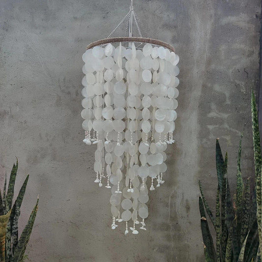 Decorative chandelier with white circular elements hanging against a textured wall.
